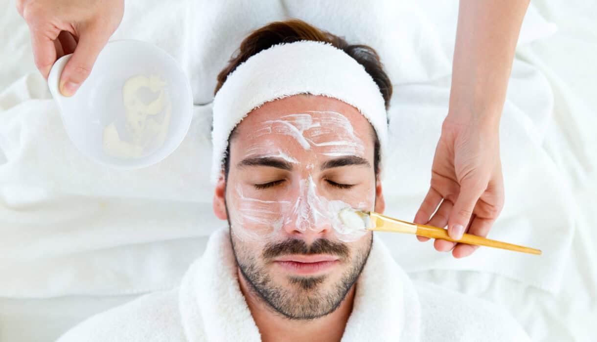 Man with clay facial mask in beauty spa.